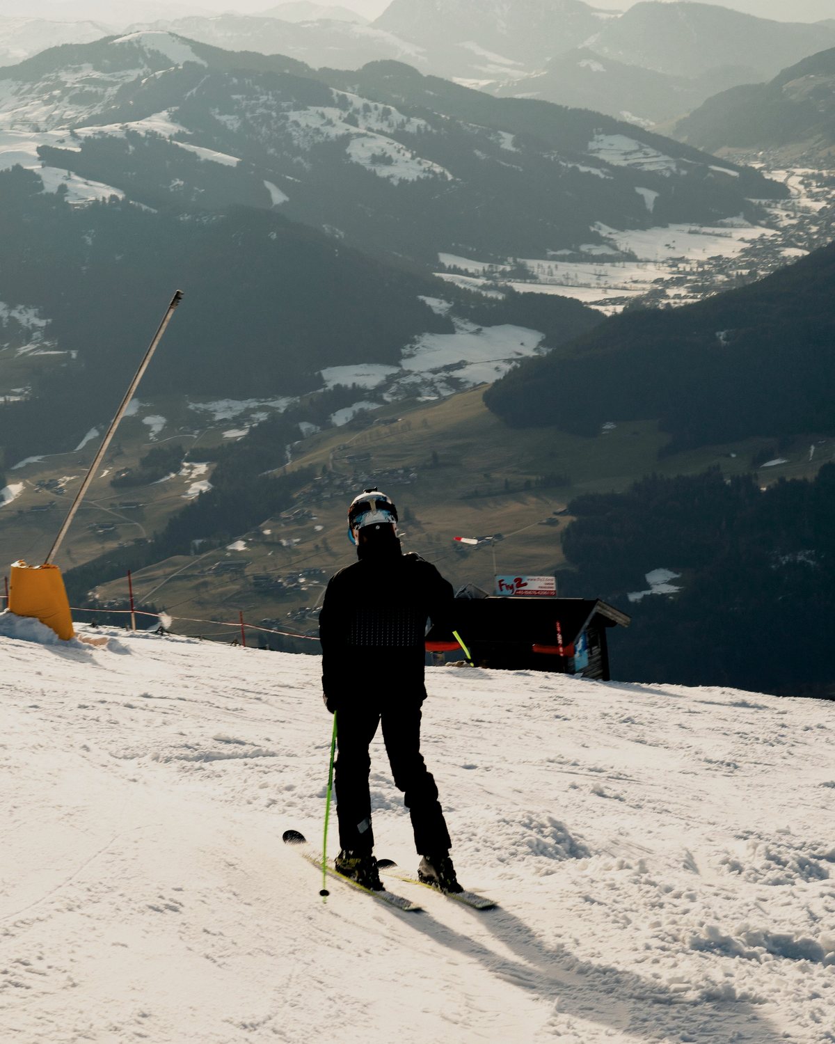 A skier standing alone at the top of a snowy slope, looking over a valley