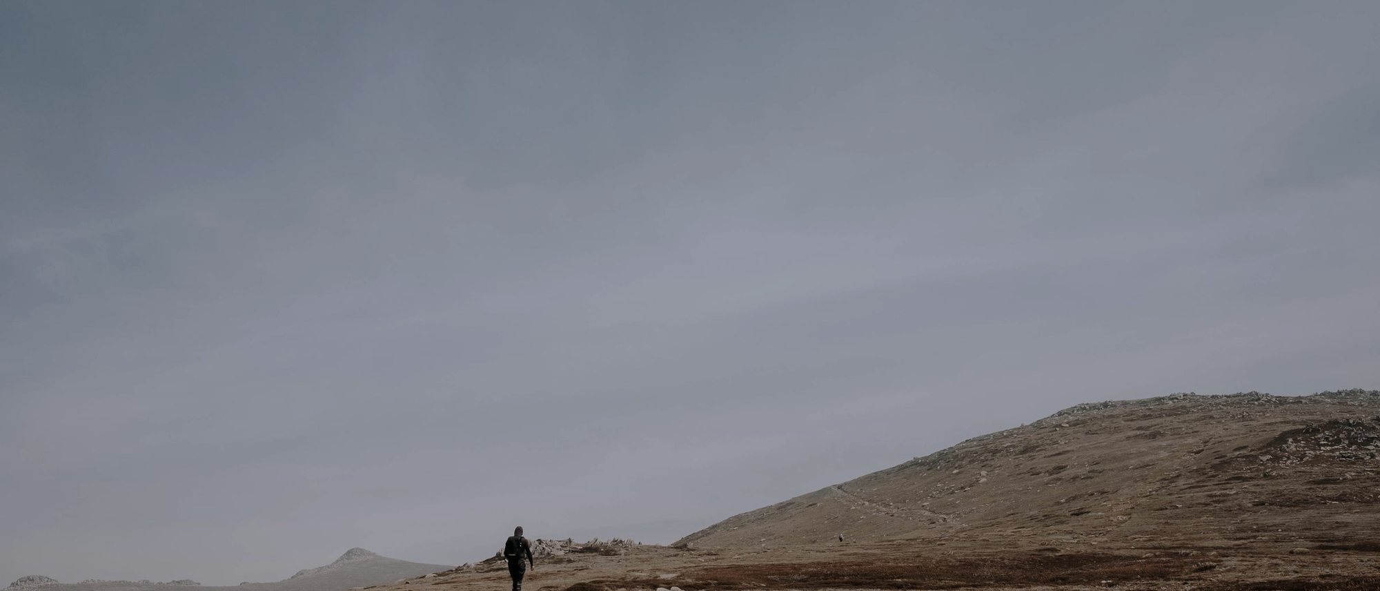 A single walker, small on a long ridge under a grey sky
