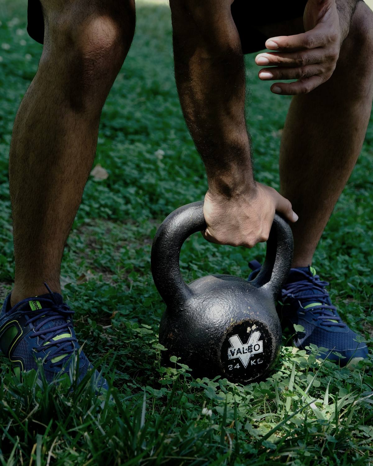 Hands gripping a kettlebell on grass, outdoors